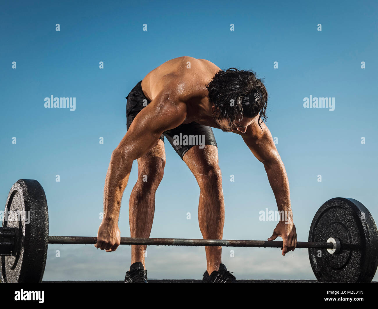 Sweating Hispanic man lifting barbell Stock Photo