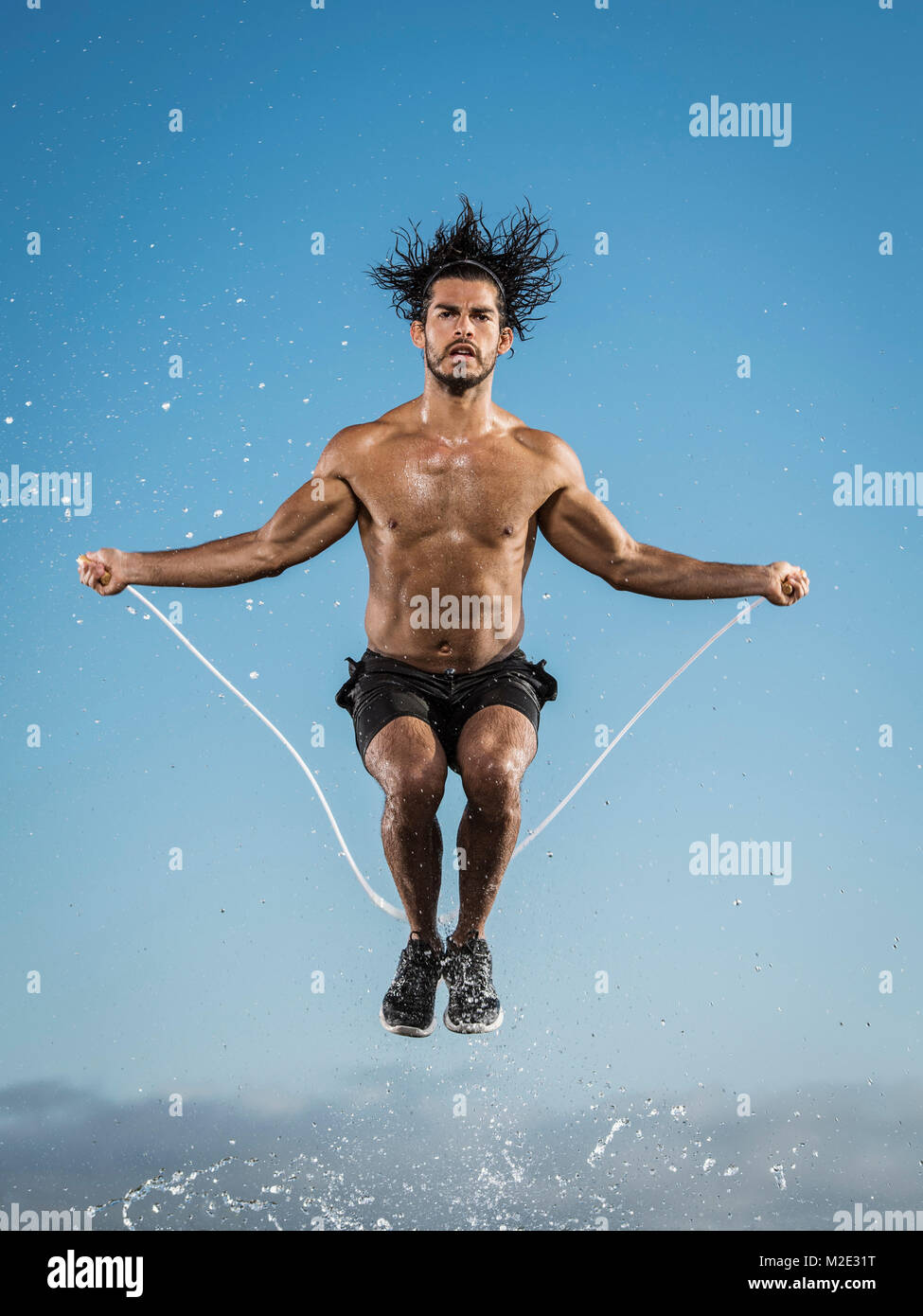Water splashing on Hispanic man jumping rope Stock Photo