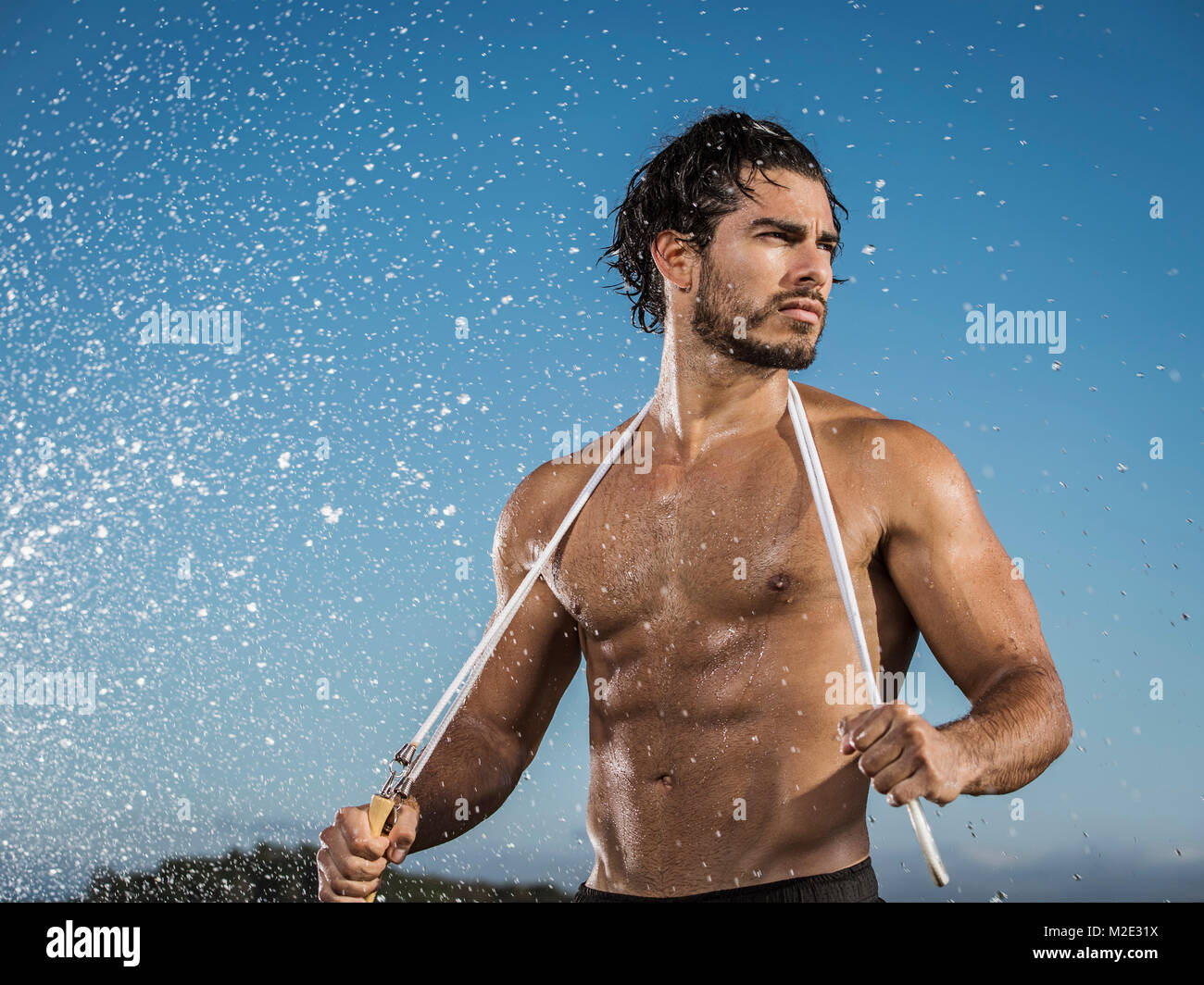 Water splashing on Hispanic man holding jump rope Stock Photo