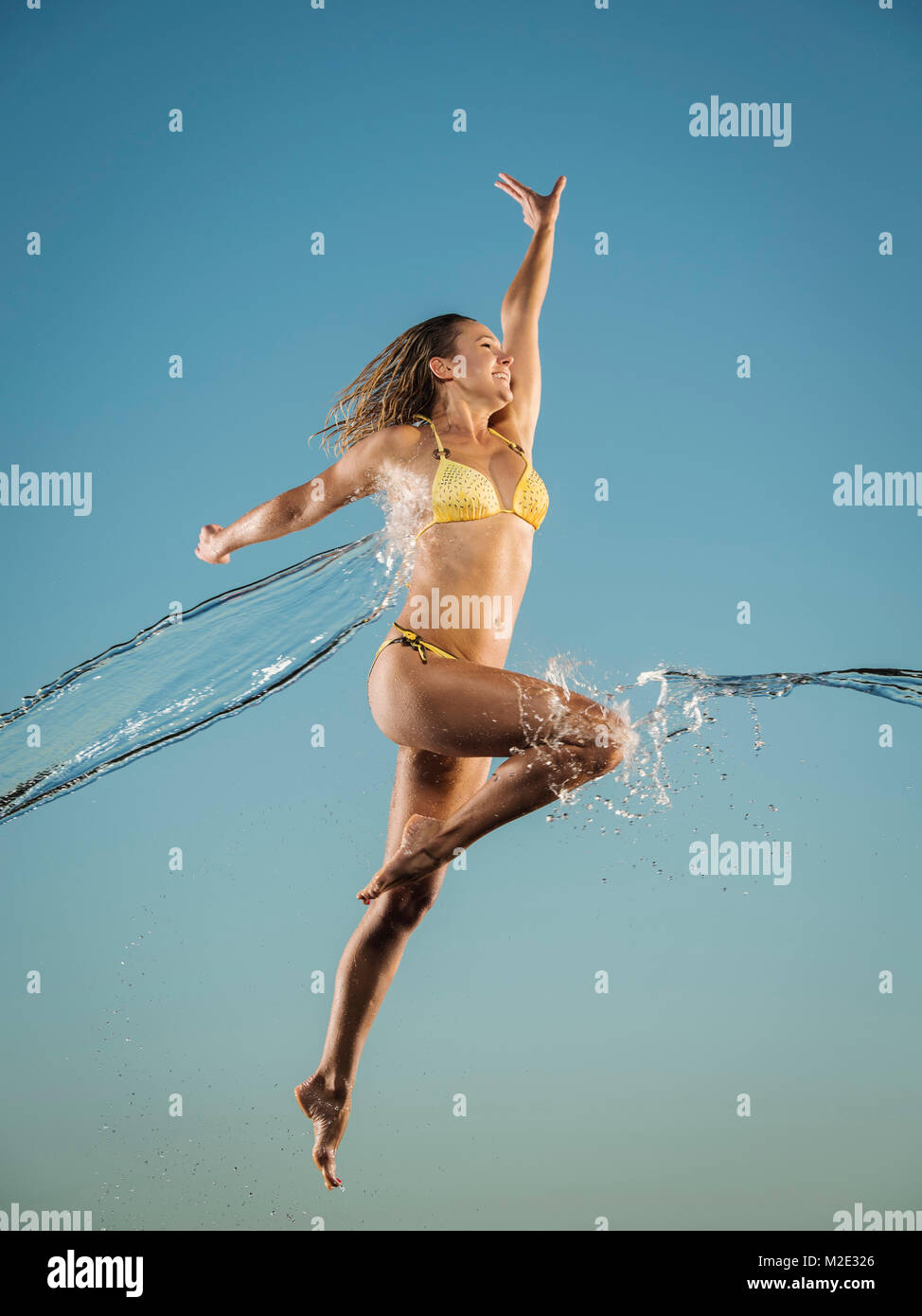 Water splashing on Caucasian woman jumping in bikini Stock Photo