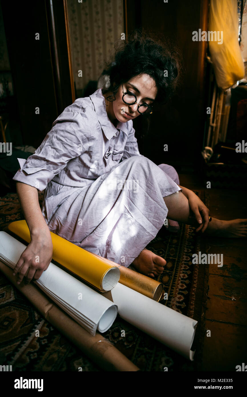 Caucasian woman sitting on floor with rolled up paper Stock Photo