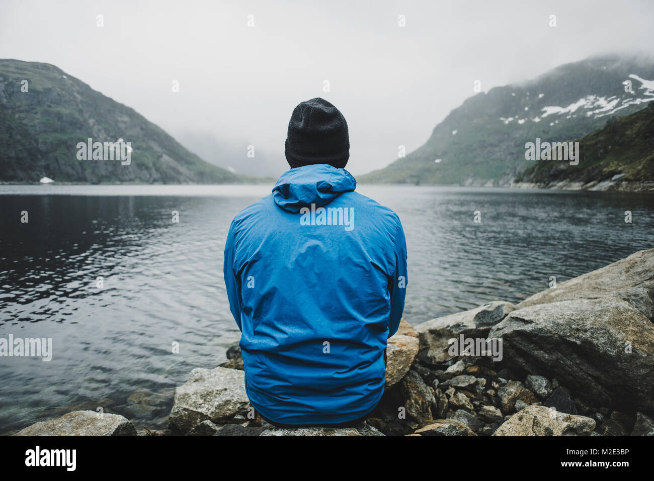 Caucasian man sitting on rocks admiring lake Stock Photo