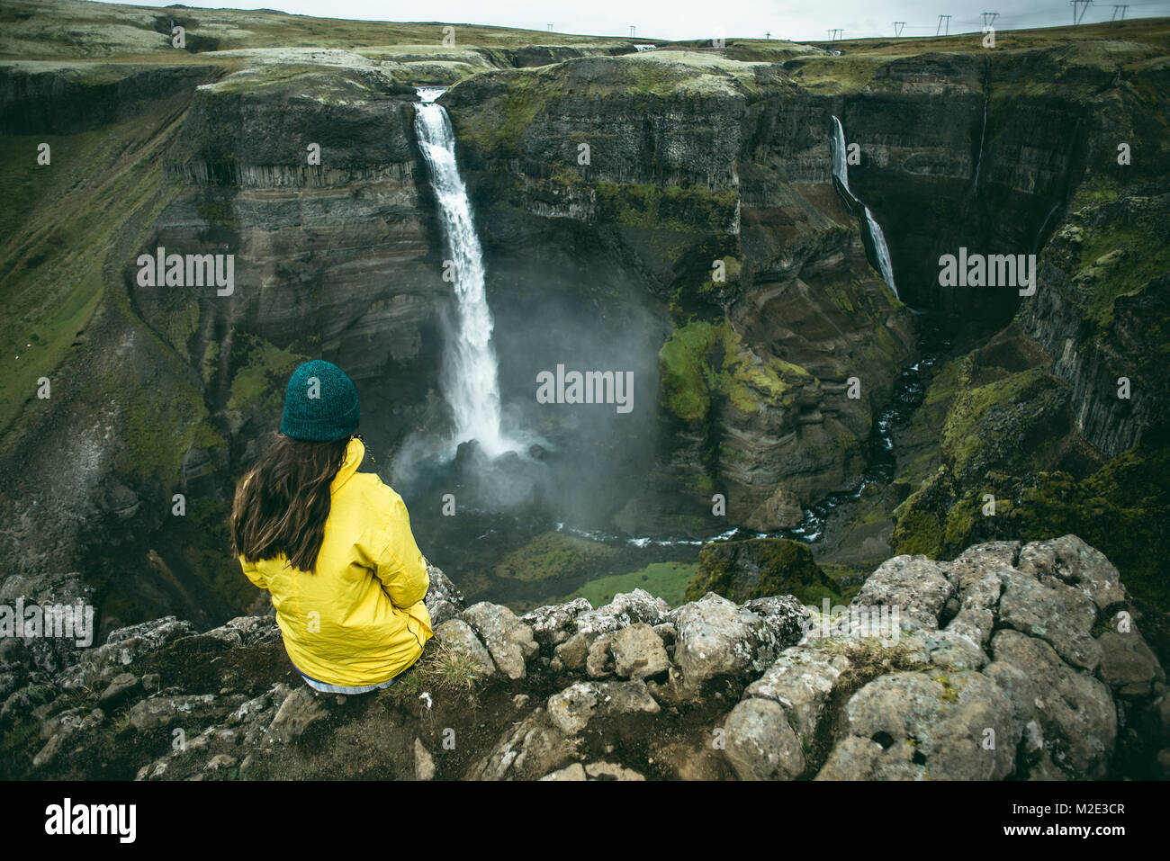 Caucasian woman sitting on cliff admiring waterfalls Stock Photo