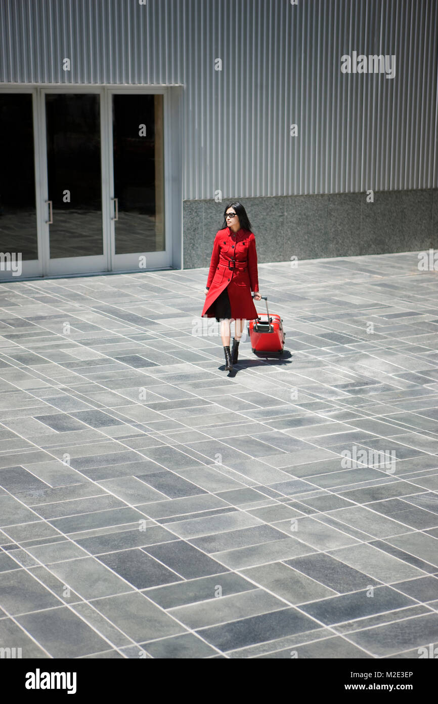Asian woman pulling rolling suitcase near building Stock Photo