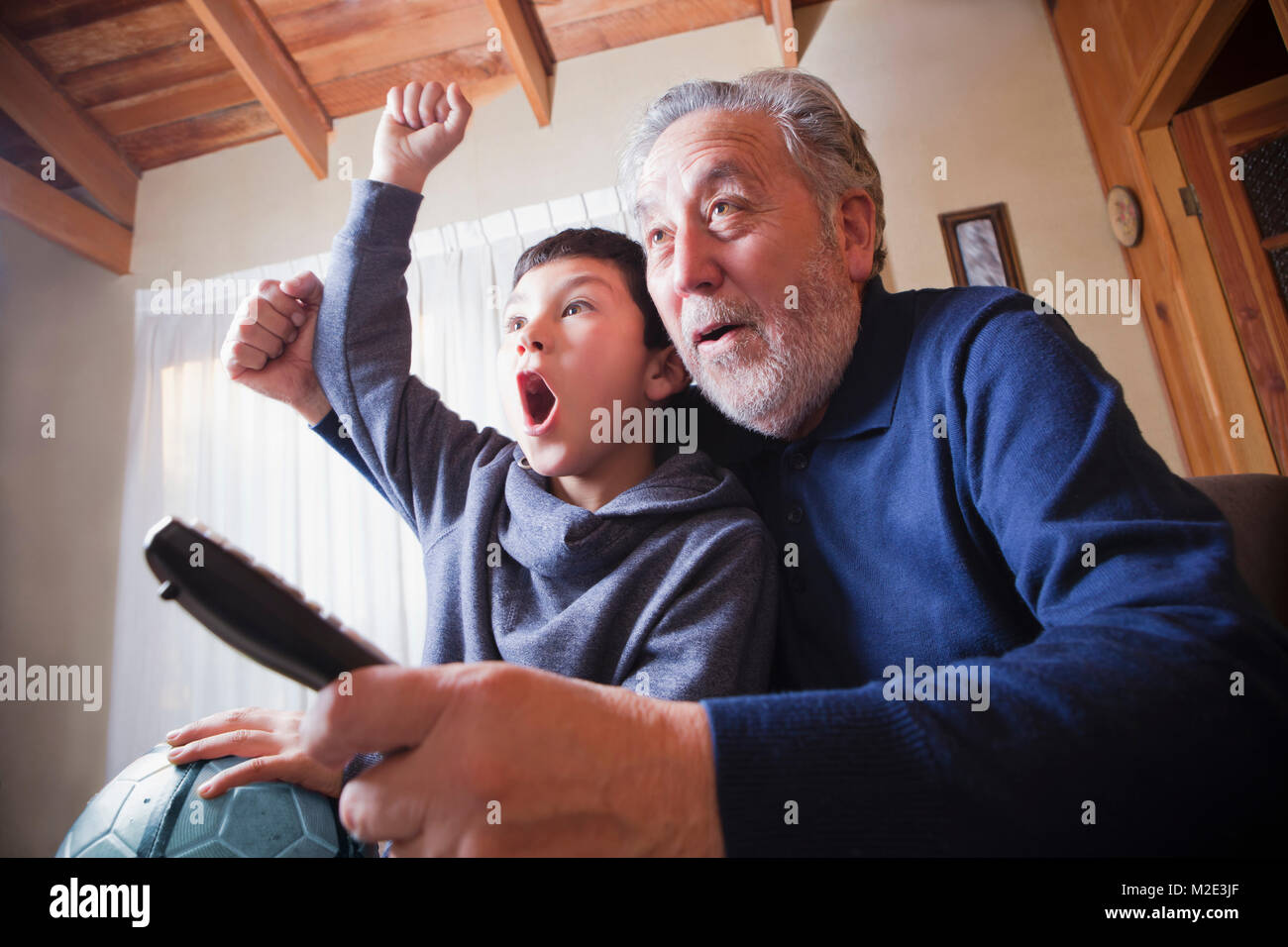 Hispanic grandfather and grandson cheering for soccer game on television Stock Photo