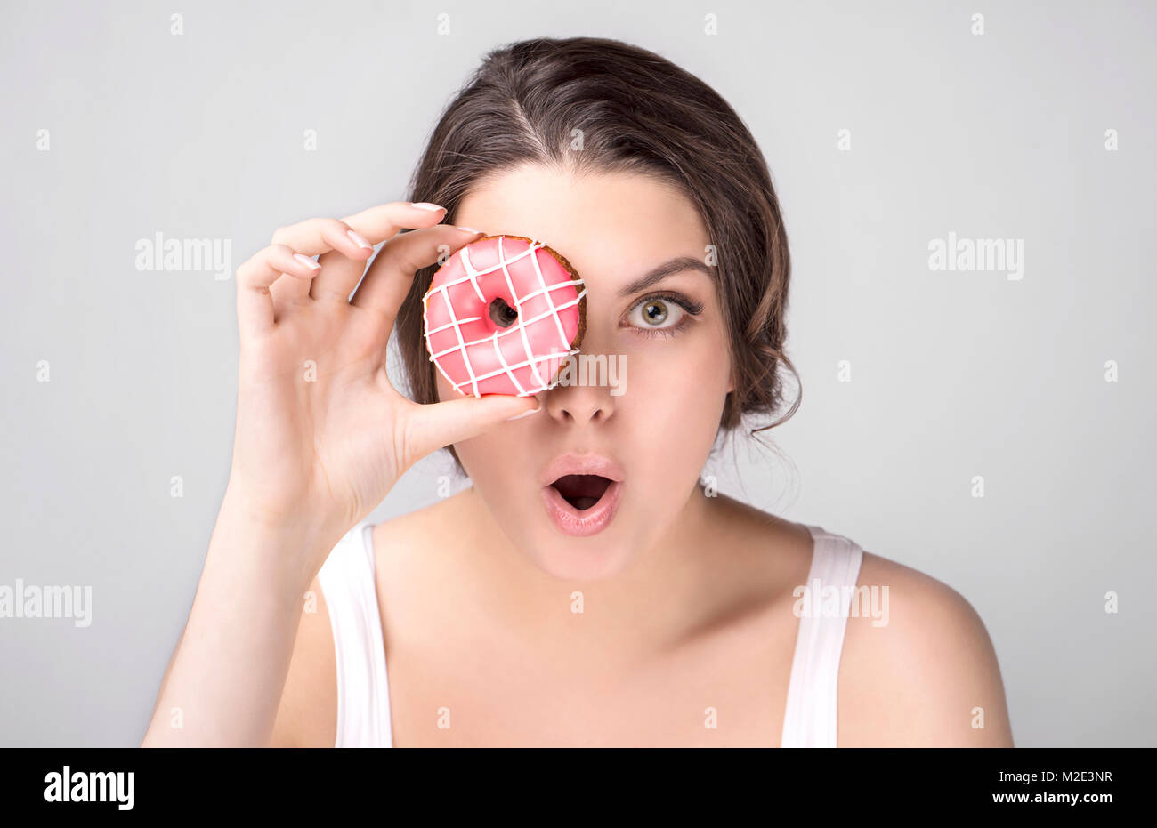 Surprised Caucasian woman holding donut over eye Stock Photo