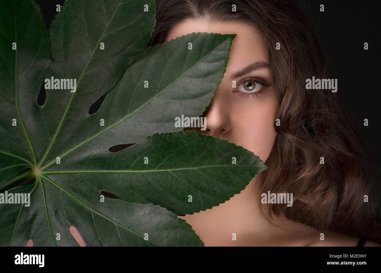 Caucasian woman hiding behind green leaf Stock Photo