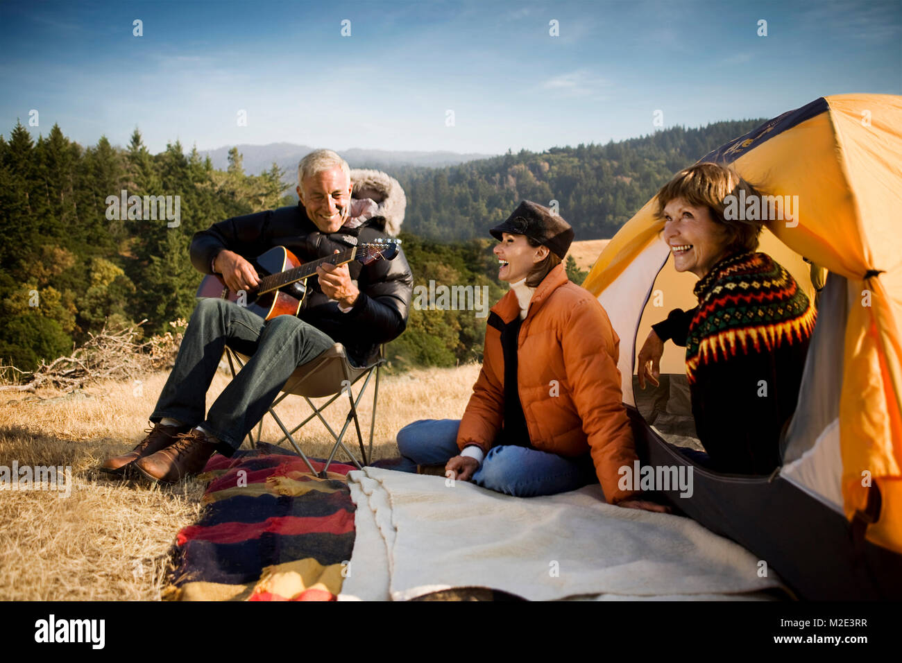 Women at camping tent listening to man playing guitar Stock Photo
