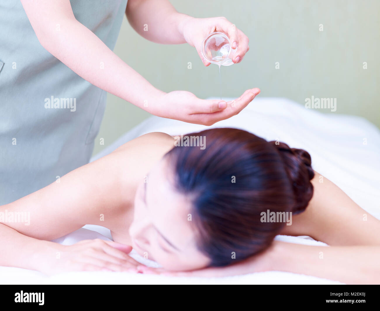 masseuse pouring essential oil on hand while young asian woman lying on front on massage bed. Stock Photo