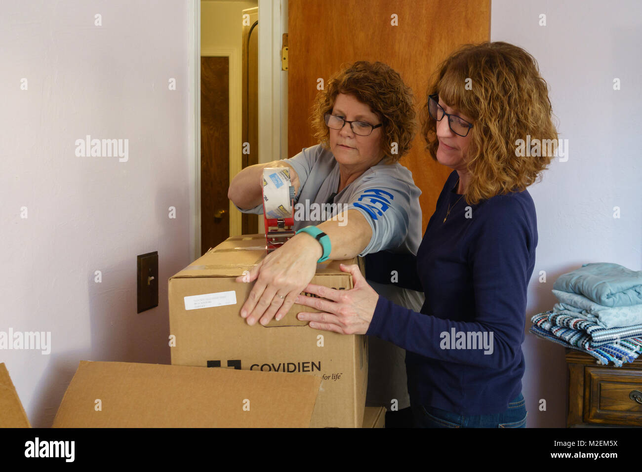 Two Caucasian women work together to tape a moving box shut in preparation to moving out of town. Oklahoma, USA. Stock Photo