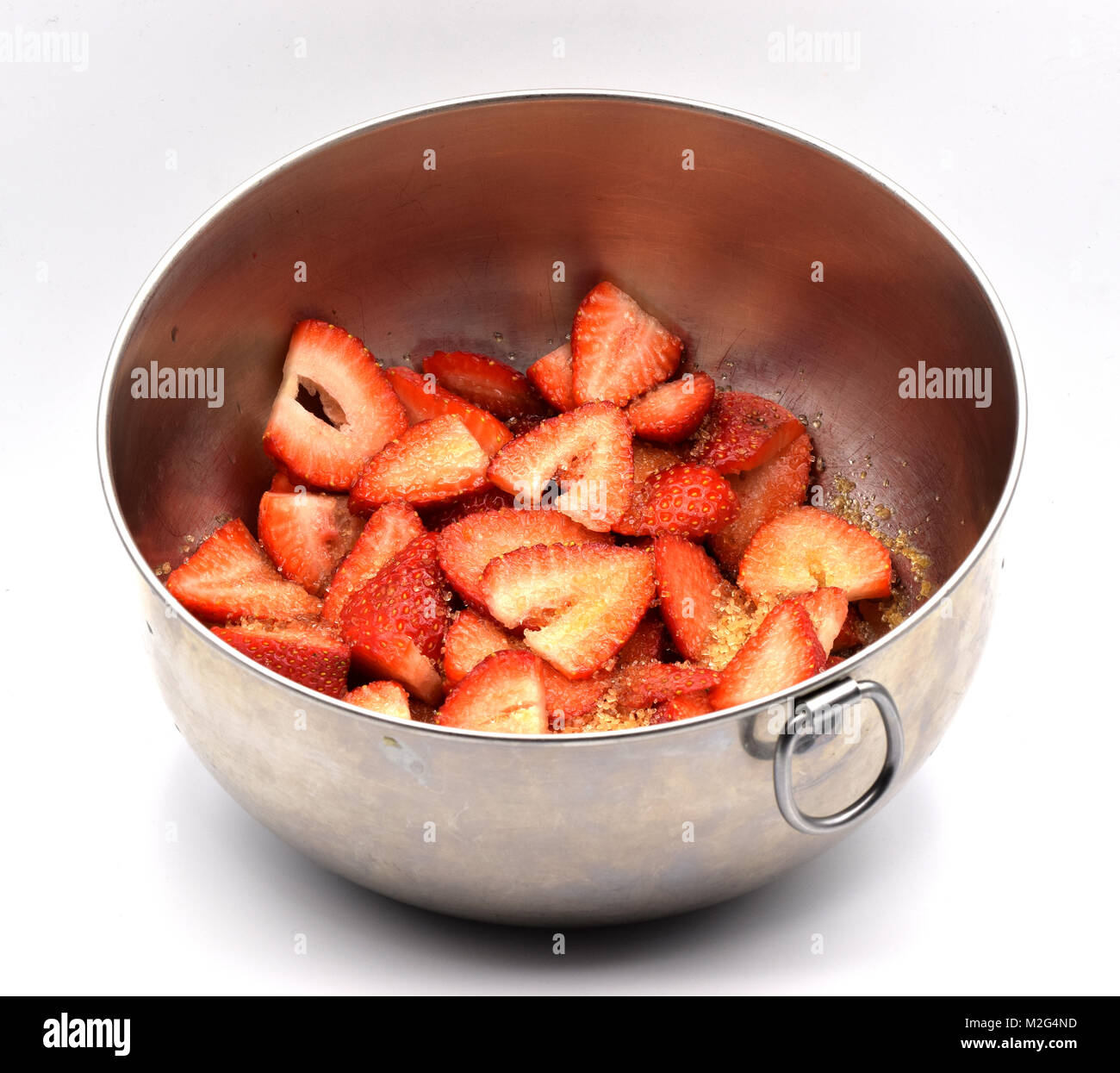 Cut strawberries covered with sugar in a metal bowl on a seamless white ...