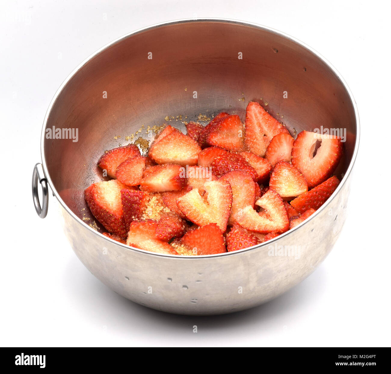 Cut strawberries covered with sugar in a metal bowl on a seamless white ...