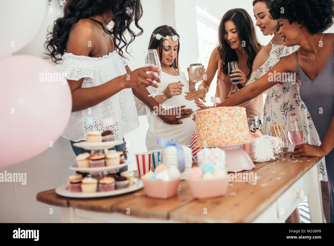 Group of female friends touching tummy of a pregnant woman at a baby shower. Female friends sharing love and support to pregnant woman. Stock Photo