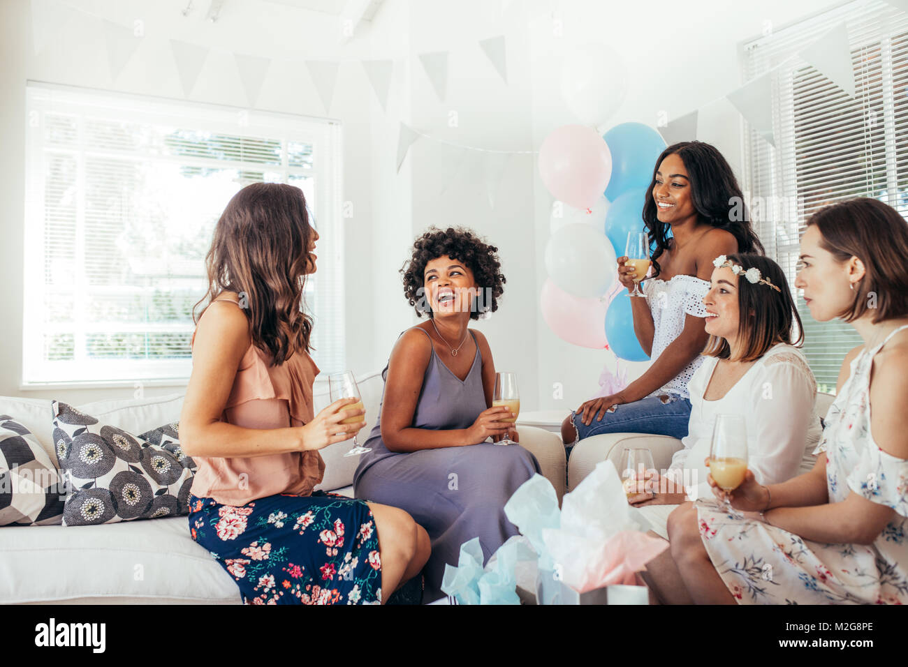 Multiracial women sitting together at a baby shower and laughing. Female friends having fun at baby shower. Stock Photo