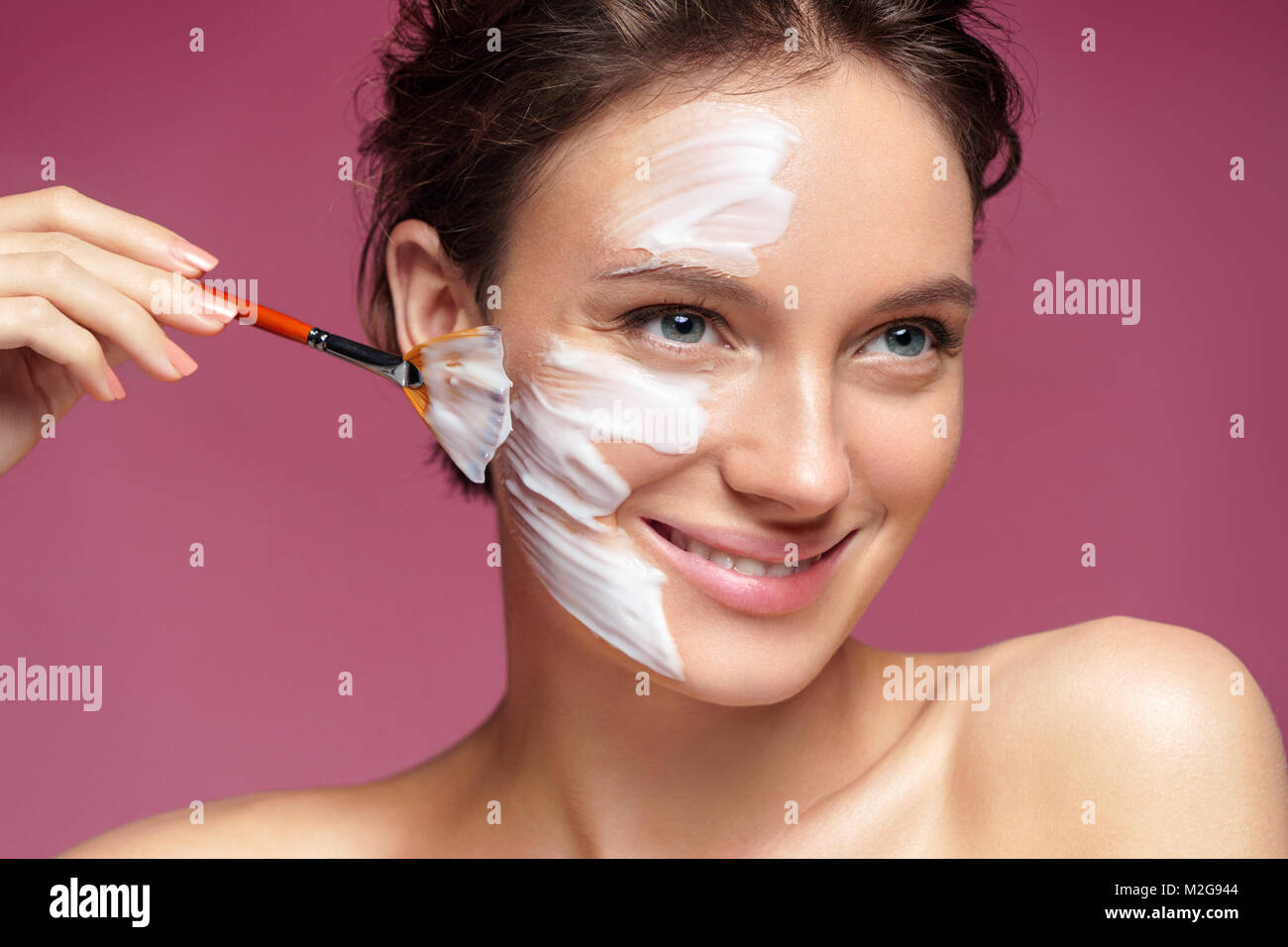 Woman with moisturizing facial mask and hands of the beautician on pink background. Photo of pretty woman receives the spa treatments. Beauty & Skin c Stock Photo