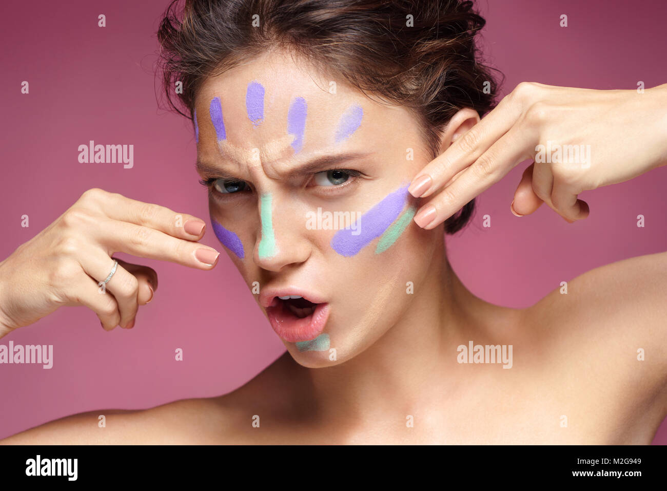Resolute woman doing makeup using concealer. Photo of beautiful brunette woman on pink background. Skin care concept Stock Photo