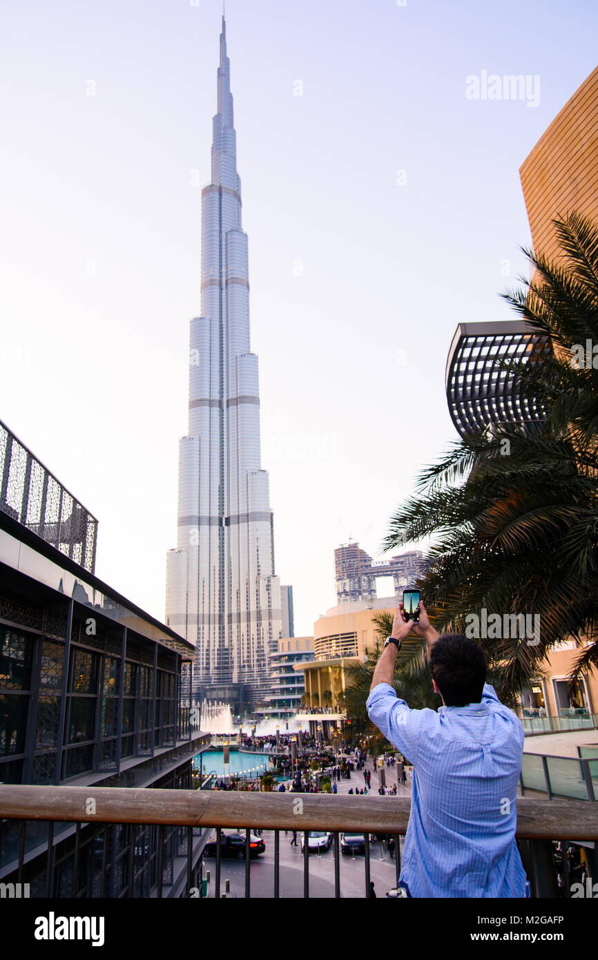 DUBAI, UNITED ARAB EMIRATES - FEBRUARY 5, 2018: Tourist taking picture of Burj Khalifa skyscraper and the fountain with smart phone at dusk Stock Photo
