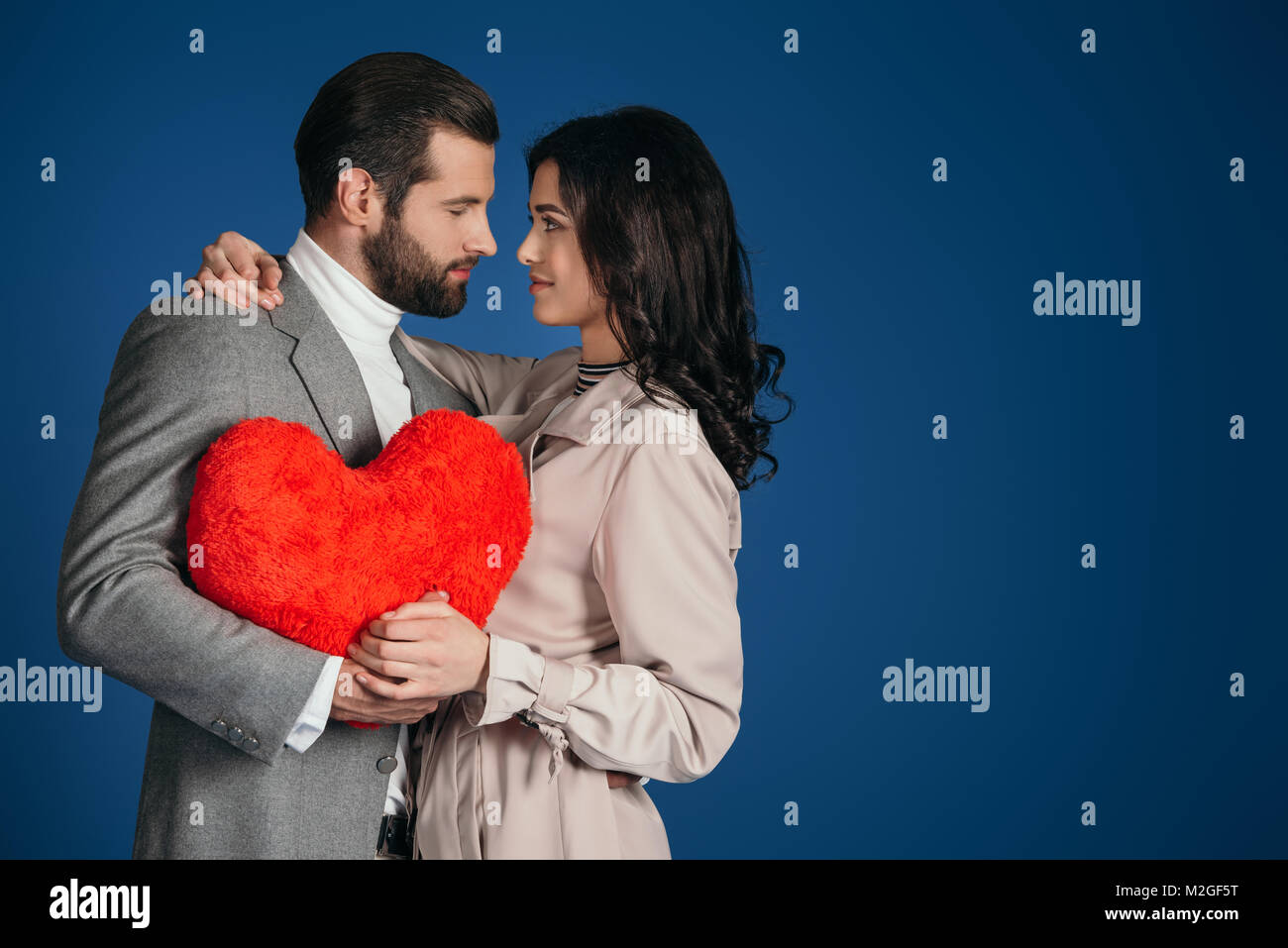 couple holding heart shaped pillow and looking at each other isolated ...