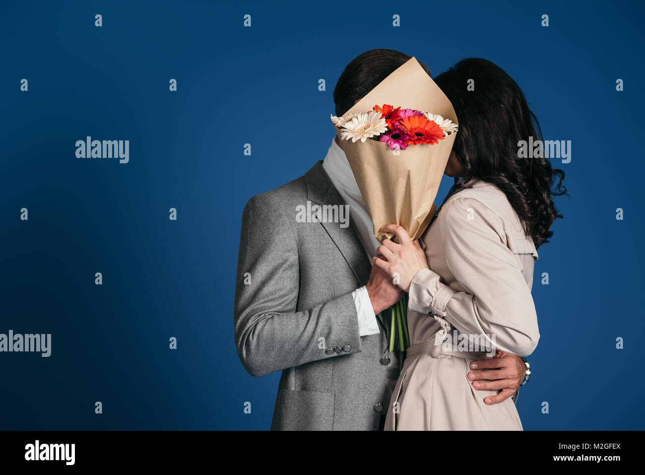 couple covering faces with bouquet isolated on blue Stock Photo