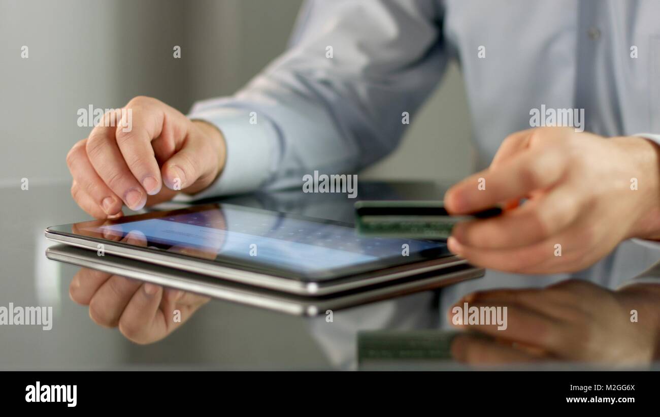 Male hands making online noncash payment on tablet, inserting bank card ...