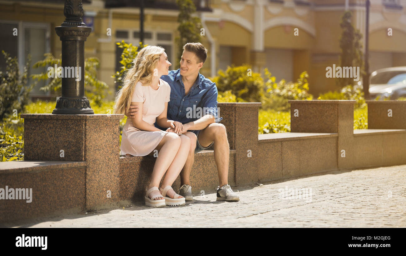 Young couple sitting on bench and holding hands, guy in love hugging ...