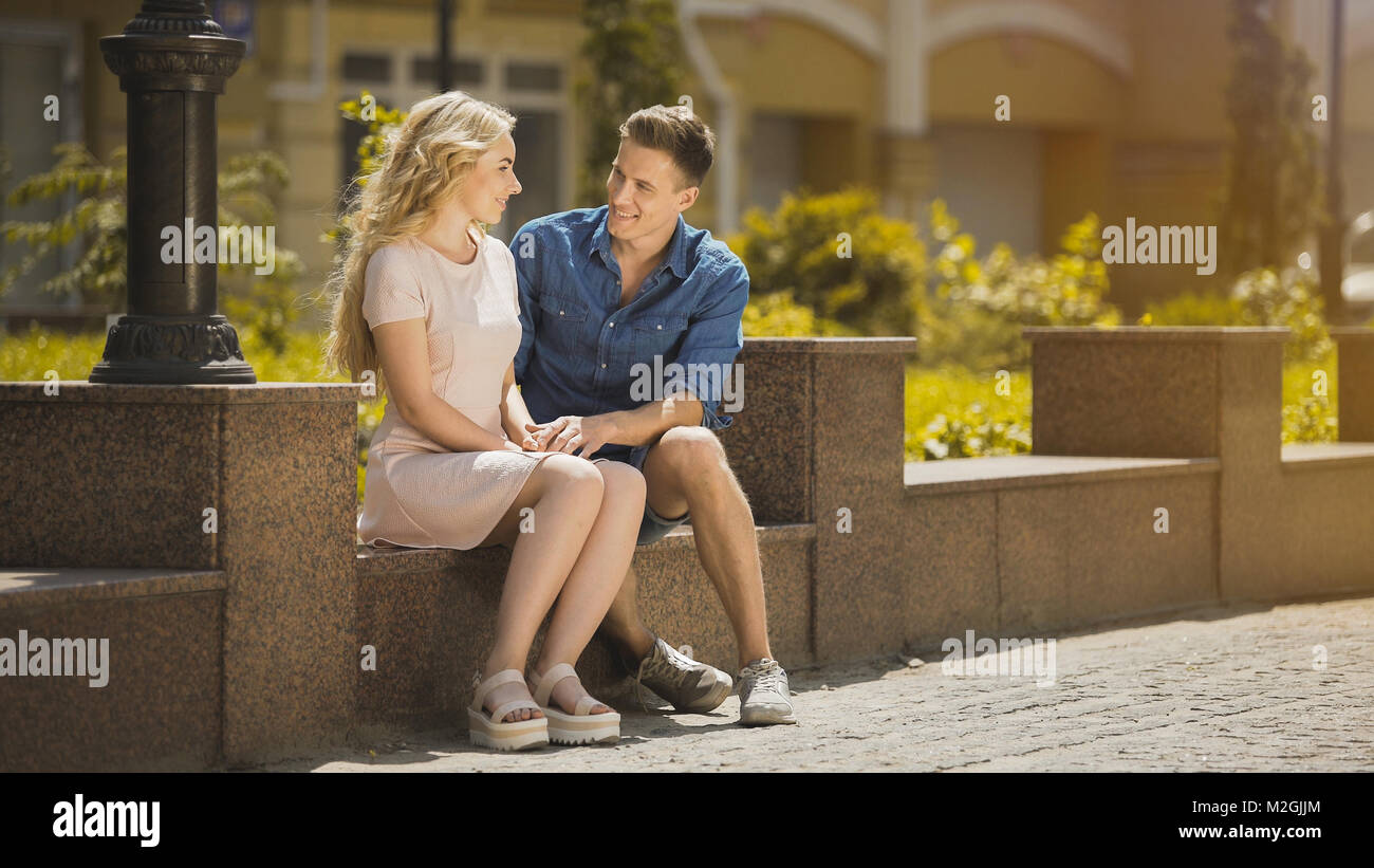 Couple sitting on bench, guy admiring blonde girl at first date, romantic mood, stock video Stock Photo