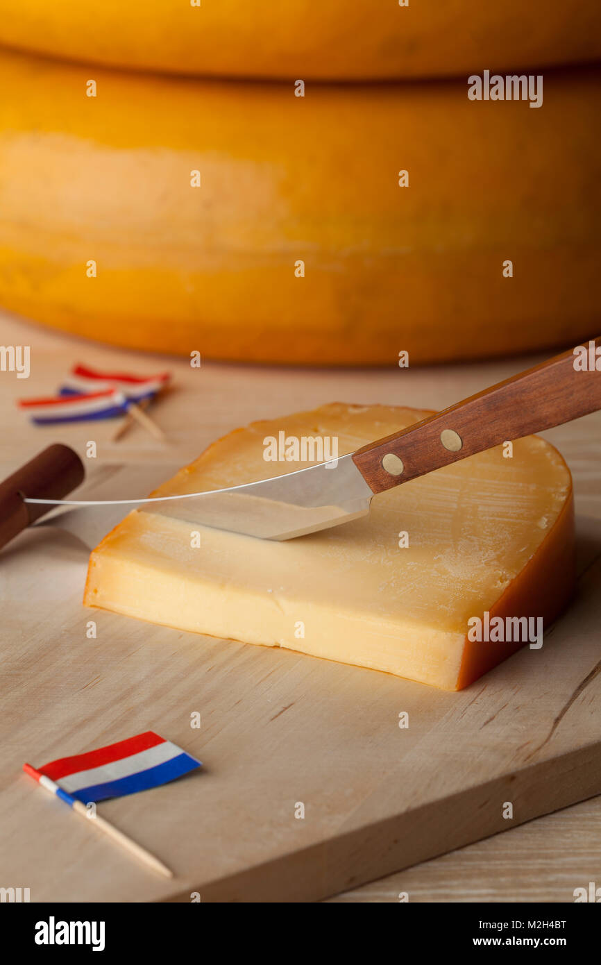Piece of Dutch mature Gouda cheese on a cutting board with flags as cocktail picks Stock Photo