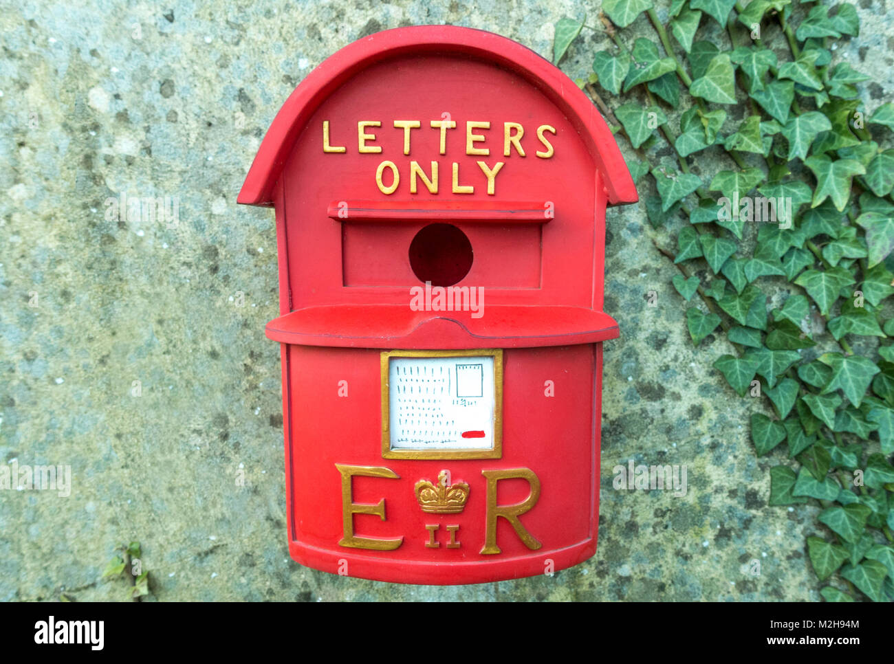 Novelty red bird box for nesting / breeding, hanging on a garden wall, resembling a British postbox, with Royal Mail Crown emblem, and 'letters only'. Stock Photo