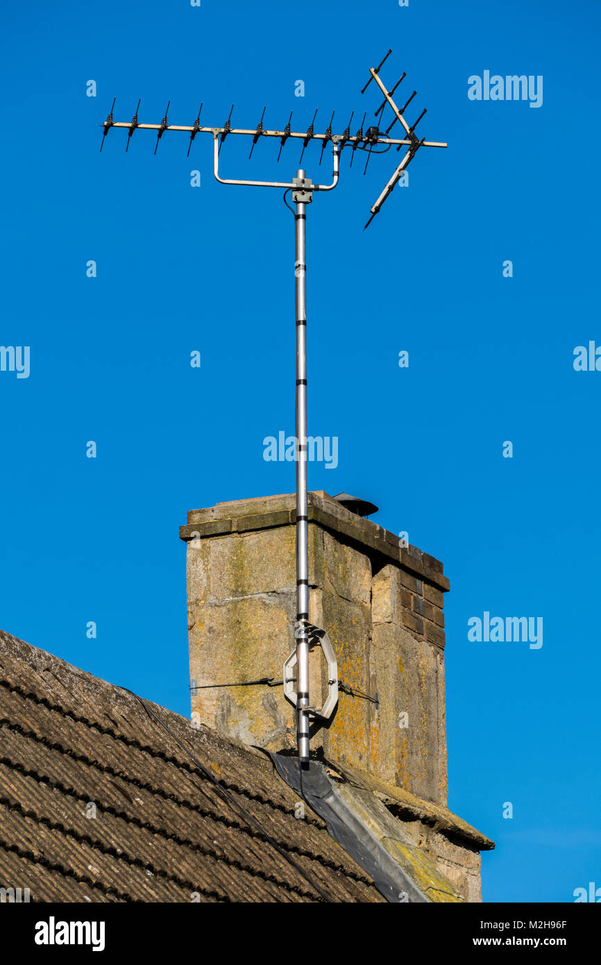 Traditionall roof aerial / antenna for television TV sound and viewing signal, attached to a roof chimney, against a blue sky. England, UK. Stock Photo