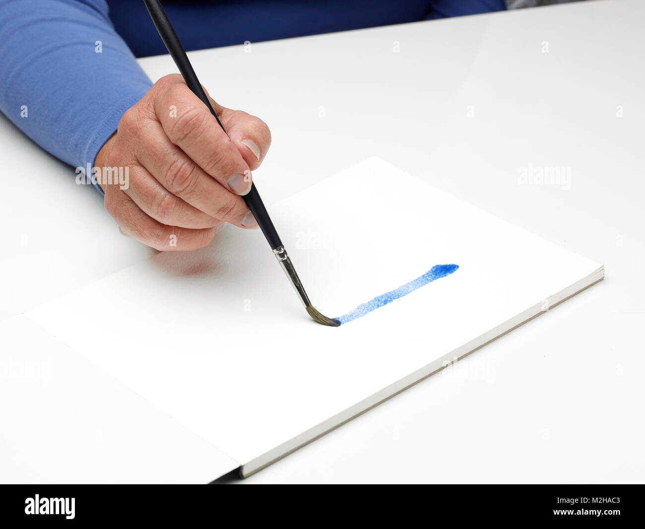 a female hand holding a brush and painting blue paint Stock Photo - Alamy
