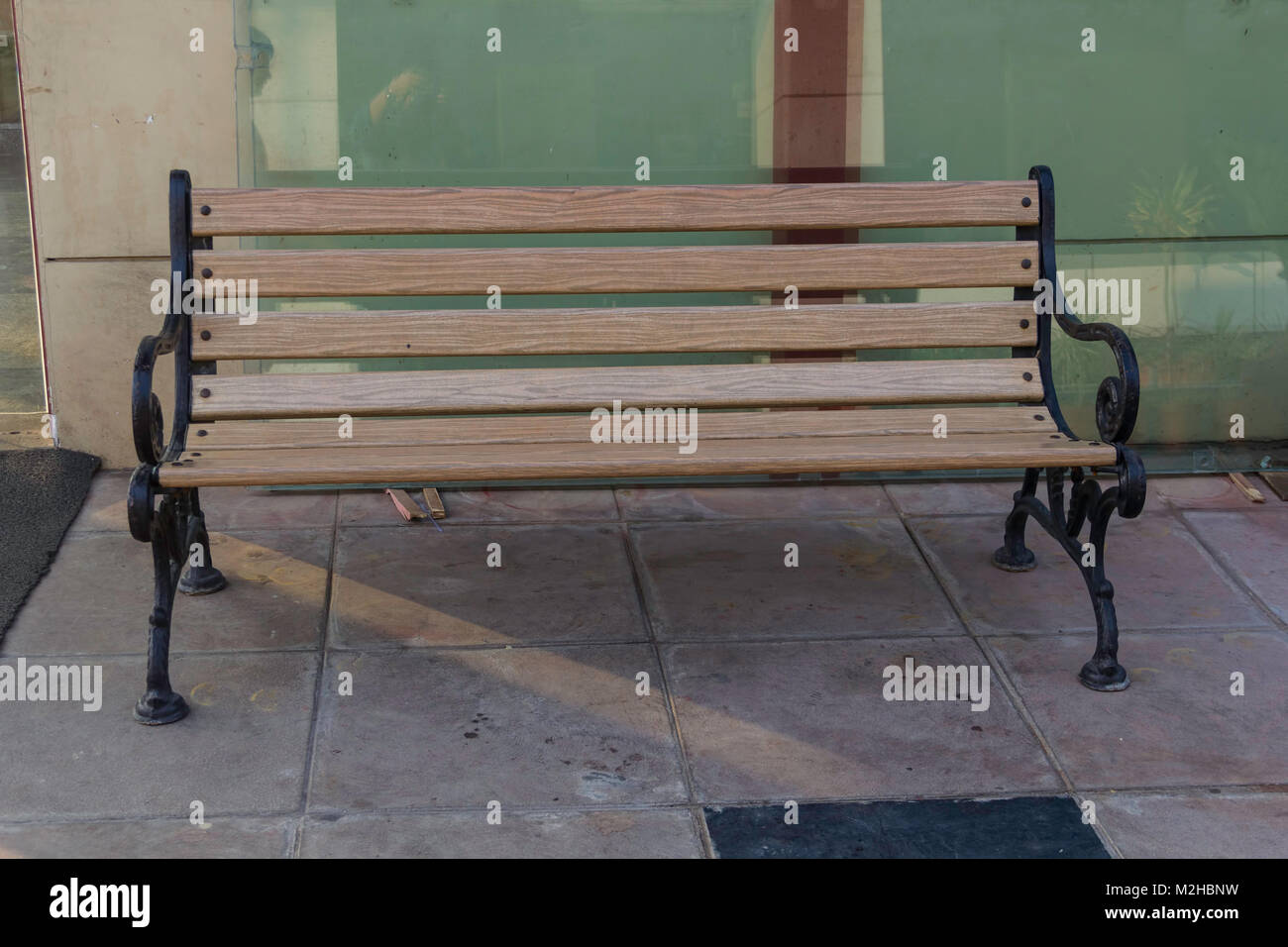 A wrought iron bench with horizontal wood strips in front of a restaurant. The glass walls of the restaurant are visible to the back of the bench. Rig Stock Photo