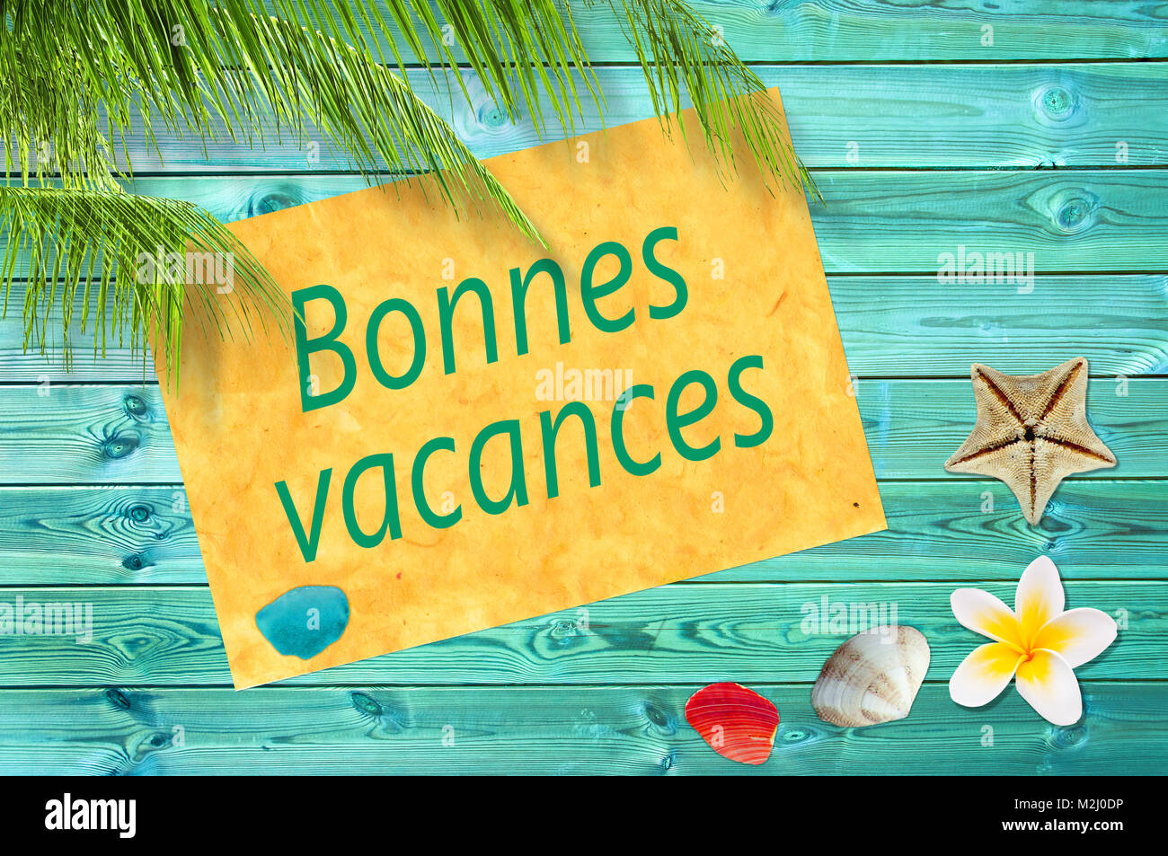 Bonnes vacances (meaning happy summer) written on a paper on colorful wood background with palm trees and sea shells Stock Photo
