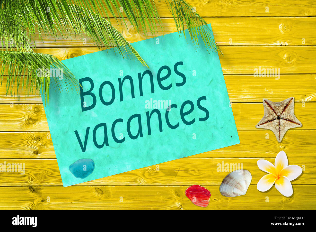 Bonnes vacances (meaning happy summer) written on a paper on colorful wood background with palm trees and sea shells Stock Photo