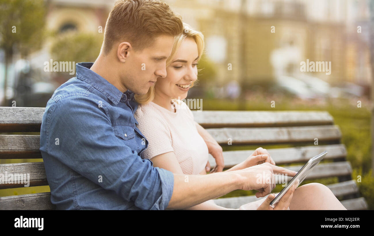 Girlfriend and boyfriend sitting on bench, using tablet, choosing place to go, stock video Stock Photo