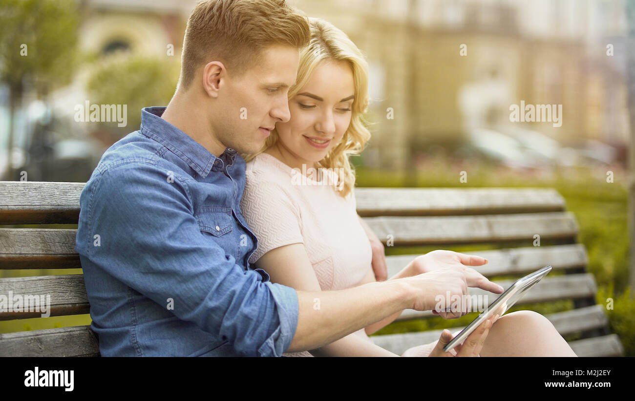 Students in love sitting on bench, using laptop, choosing where to spend summer, stock video Stock Photo