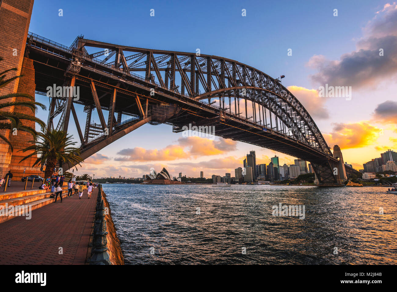 People walk under the Harbour Bridge with view of Sydney skyline Stock Photo
