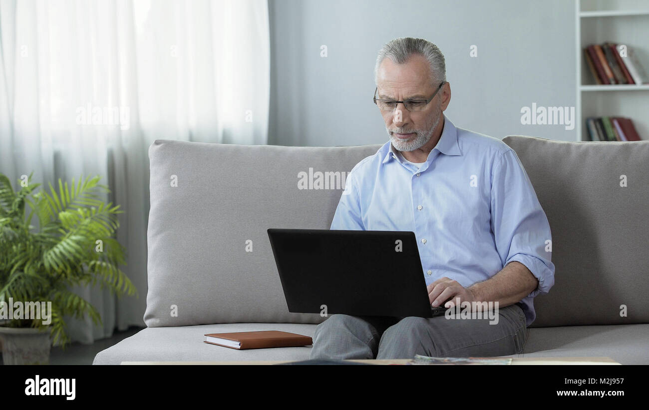 Male journalist sitting on couch and working on laptop, freelance and