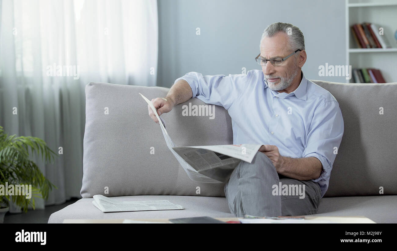 Senior male sitting on sofa and reading newspaper, press and news, rest time, stock footage Stock Photo