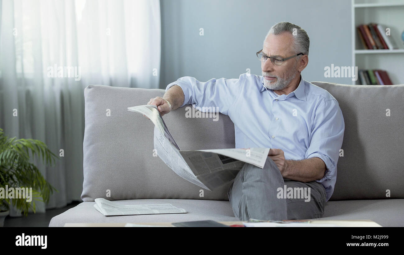 Man in his 60s sitting on couch and reading newspaper, morning ritual, press, stock footage Stock Photo