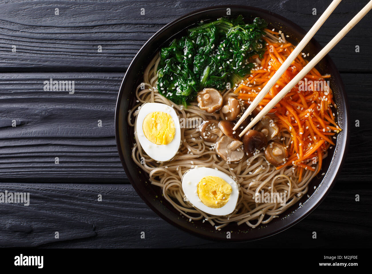 Asian Soba soup with vegetables, mushrooms, egg and sesame seeds close up in a bowl. horizontal top view from above Stock Photo