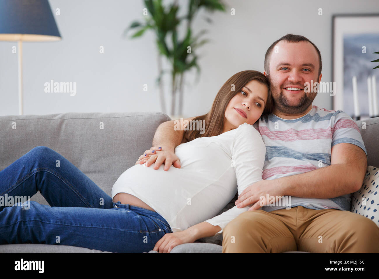 Photo of happy future parents sitting on gray sofa Stock Photo