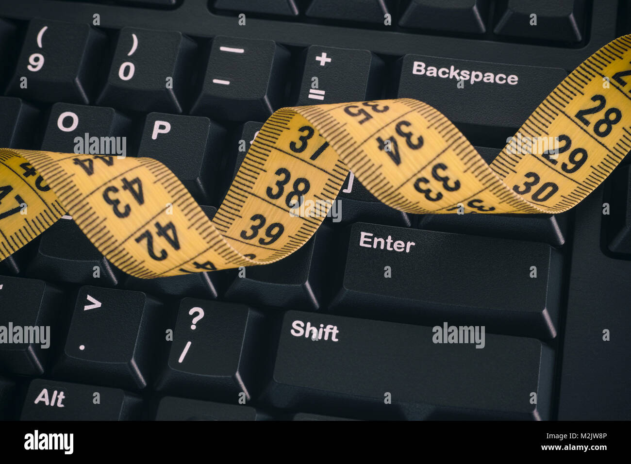 Black computer keyboard and yellow tape measure. Close up. Stock Photo