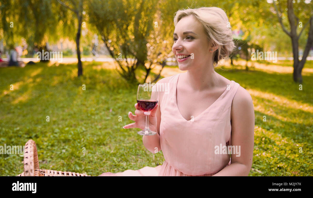 Pretty girl sipping wine in shade of park trees spending wonderful time in park Stock Photo