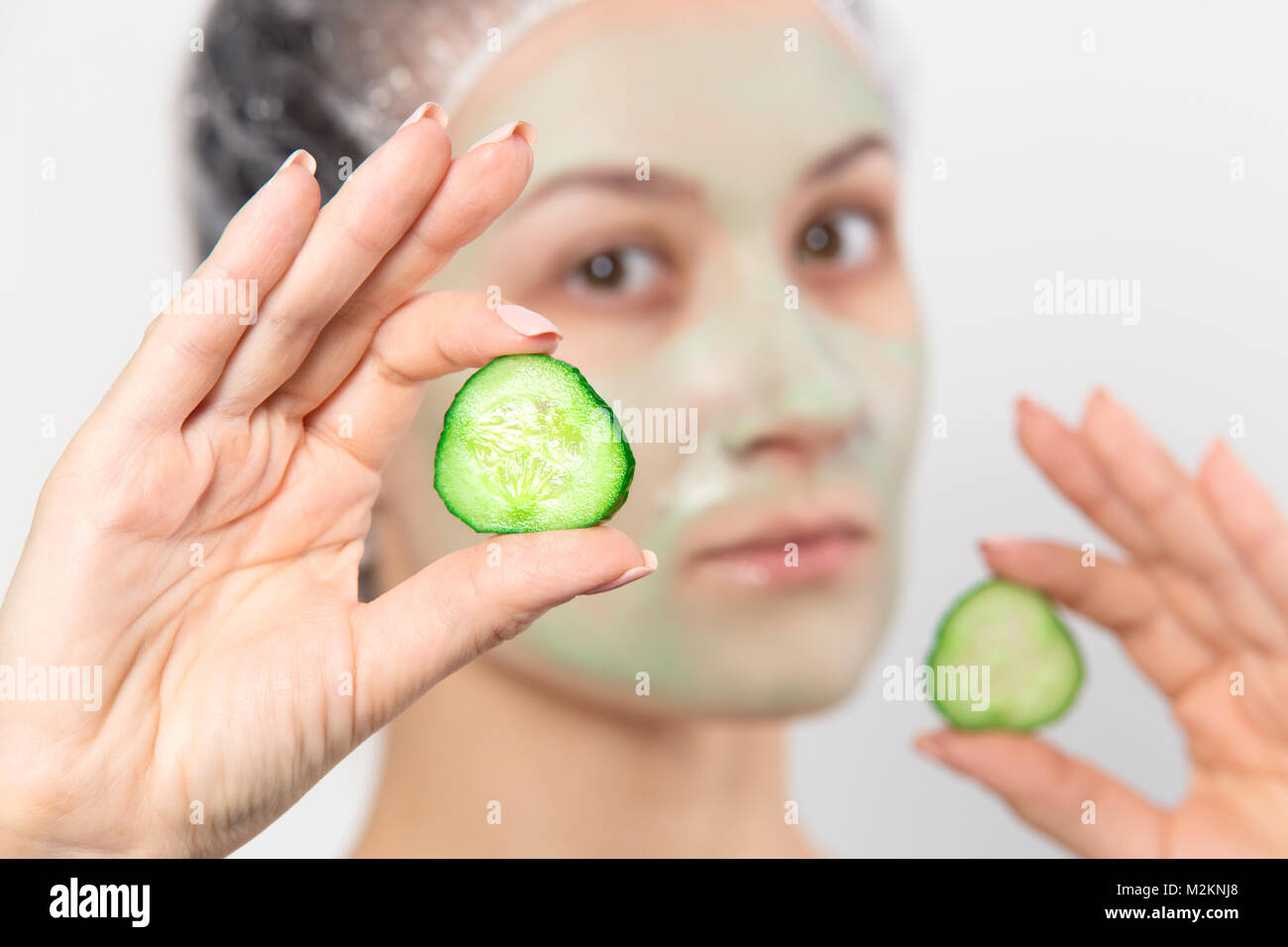 Woman with green cucumber mask on face holding round slices of cucumber. Facial skin care with natural mask. Healthy lifestyle background. Stock Photo