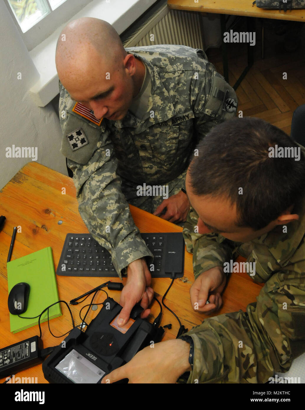 A U.S. military intelligence noncommissioned officer assigned to 1st Battalion, 10th Special Forces Group (Airborne), left, demonstrates how to use the Secure Electronic Enrollment Kit to an intel officer assigned to the Poland Special Operations Command during a training engagement sponsored by U.S. Special Operations Command Europe Aug. 11 at Panzer Barracks. The engagement is part of SOCEUR's mission to increase the SOF interoperability and capability of partner nations within European Command's area of responsibility. Military intelligence soldier assists Polish soldier with equipment by E Stock Photo