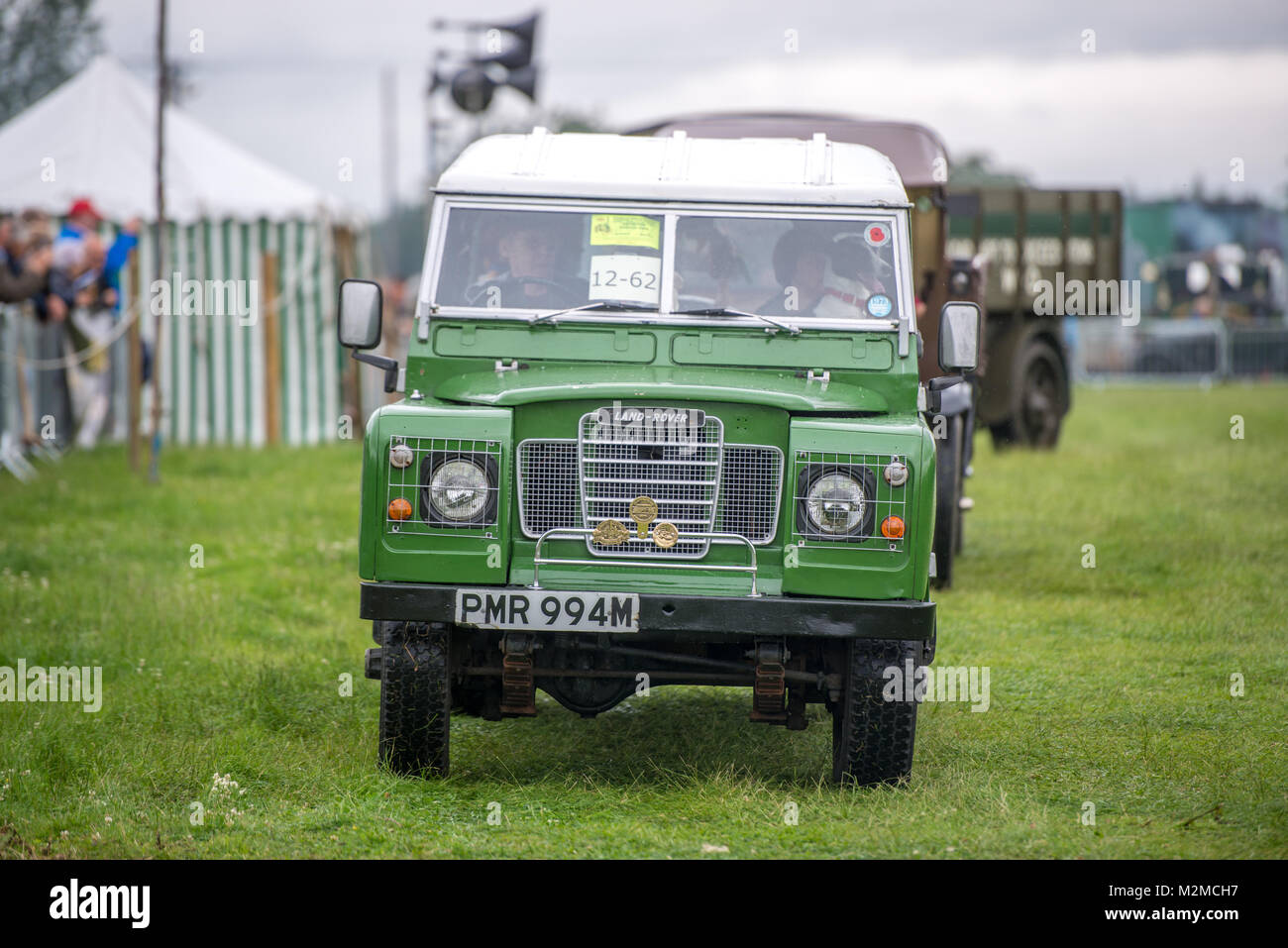Front view of vintage green Land Rover being driven along in the grass, Masham, North Yorkshire, UK Stock Photo