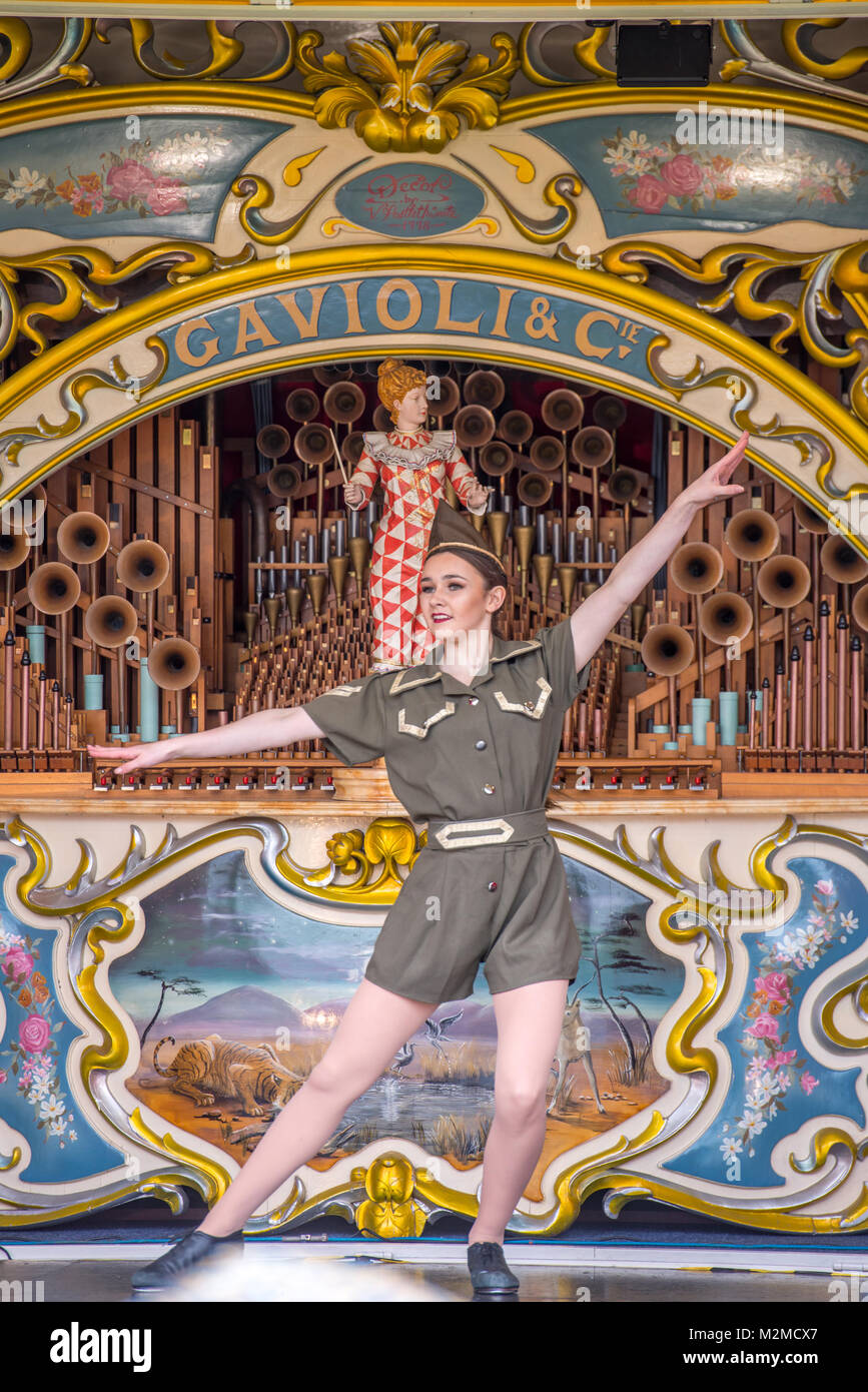 Young female dancer in military outfit showing off moves on top of fairground organ, Masham, North Yorkshire, UK Stock Photo