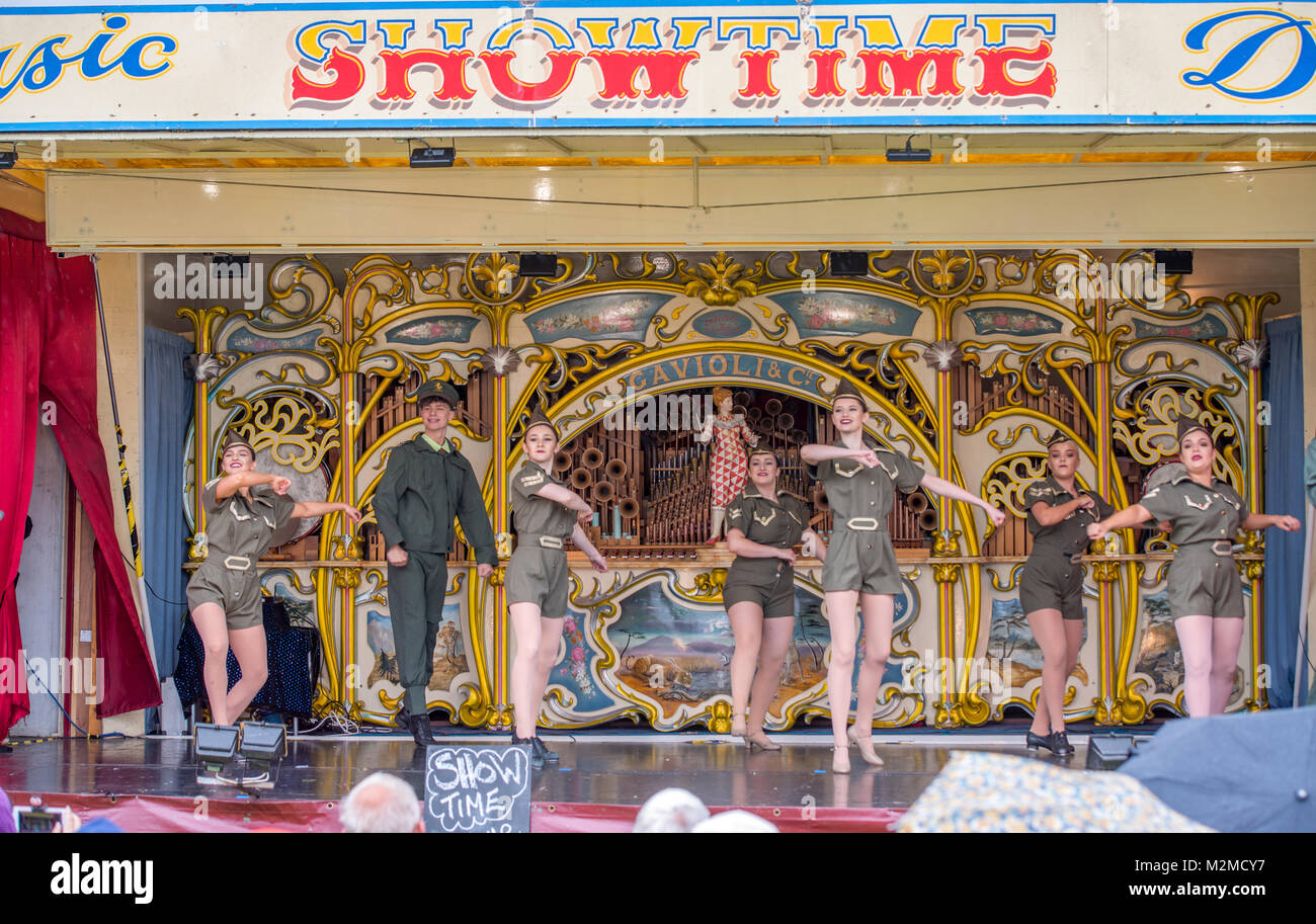 Onlookers watch young female dancers in military attire preform on fairground organ, Masham, North Yorkshire, UK Stock Photo