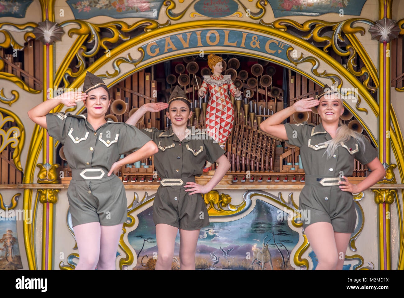 Young female dancers in military outfits stand at salute on top of fairground organ, Masham, North Yorkshire, UK Stock Photo