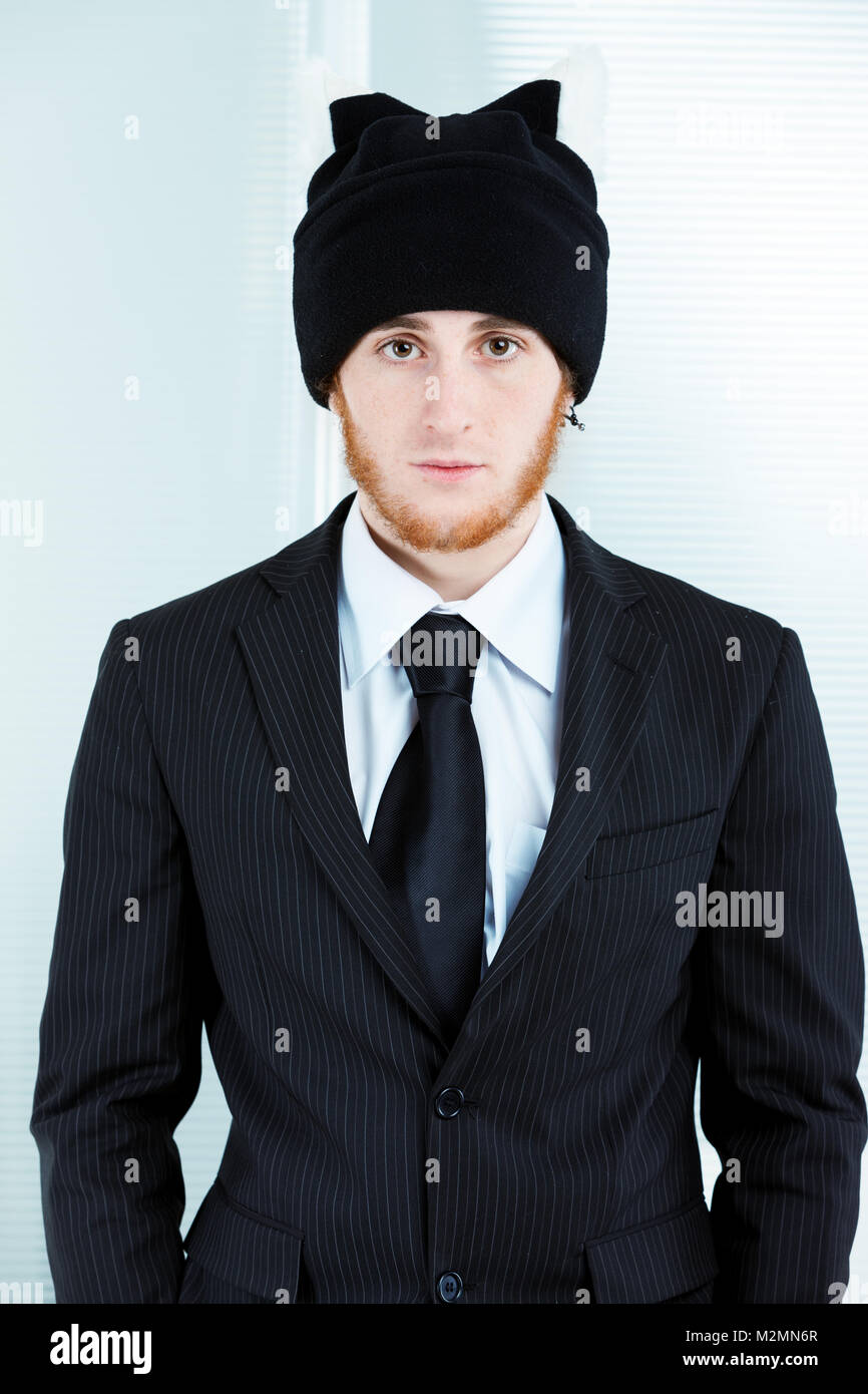 Strange businessman wearing a knitted black cap with his suit and tie staring at the camera with a deadpan expression in an isolated portrait Stock Photo